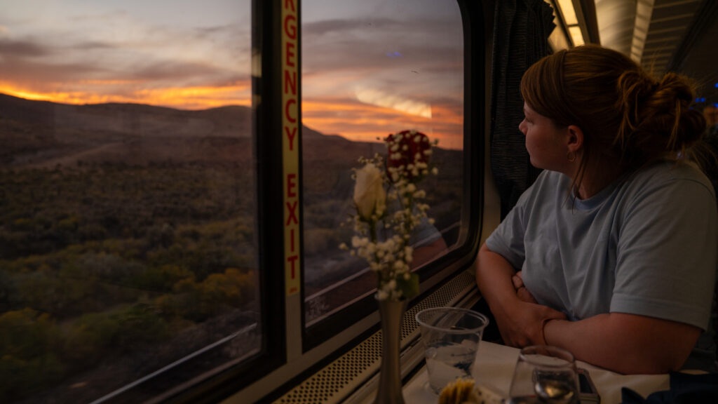 A dining companion looks out the train window toward a golden sunset behind mountains in eastern Nevada.