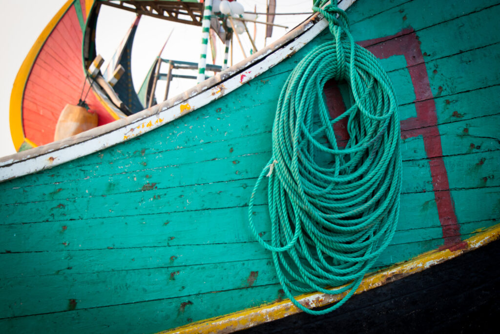 Bright green fishing rope is coiled along the side of a green moon boat, with part of a red boat visible behind it.