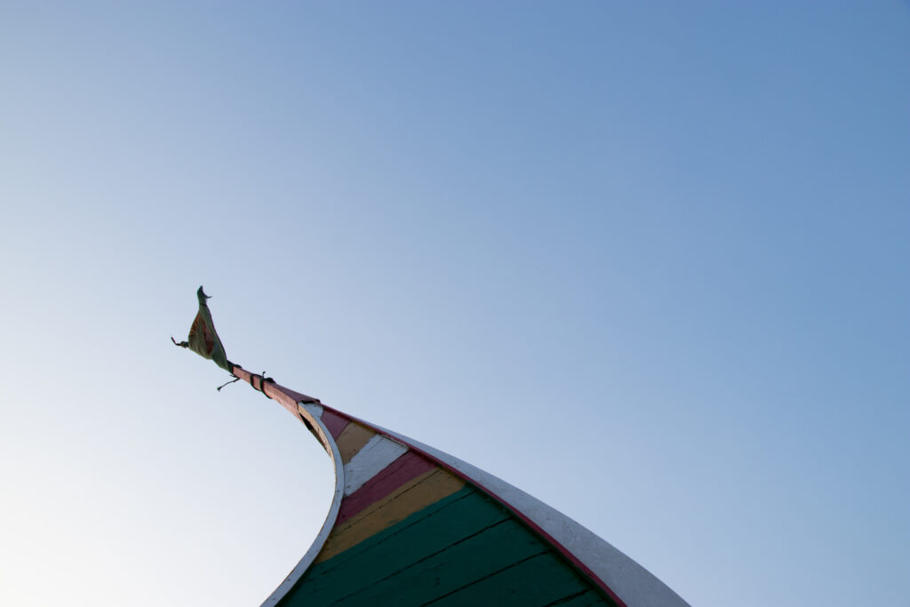 The tall curved tip of a green moon boat reaches into the blue sky with a green flag flying from its peak.