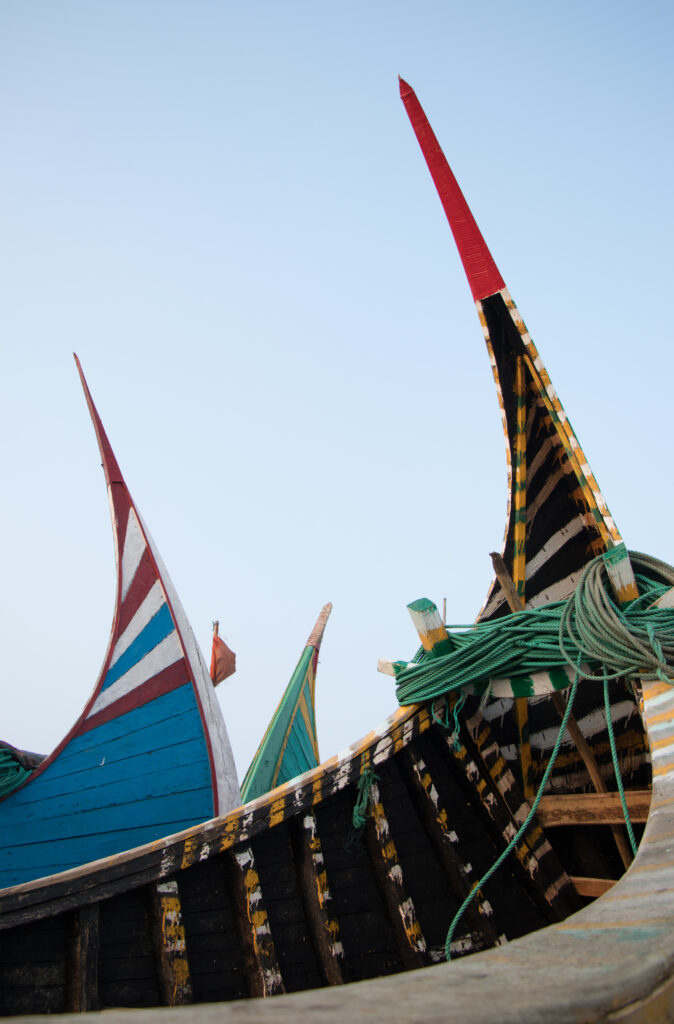 Green fishing ropes lie inside the black hull of a moon boat with yellow-and-white trim, with blue and green boats behind it.