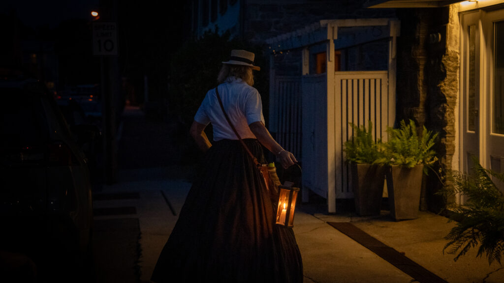 Janet Hughes carries a lantern past a historic Shepherdstown building associated with Irish railroad workers who died during a cholera outbreak.