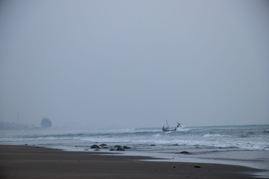 A moon boat pushes through choppy waves on the Bay of Bengal beneath a pale blue sky off southeastern Bangladesh.