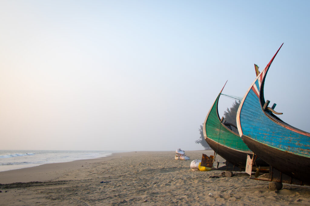 A wide sandy beach stretches toward two moon boats at right, one green and one blue with red-and-white stripes on its tip.