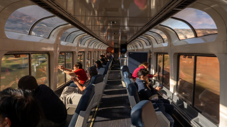 Wide view of the observation car with passengers taking photos as scenery blurs past the windows.