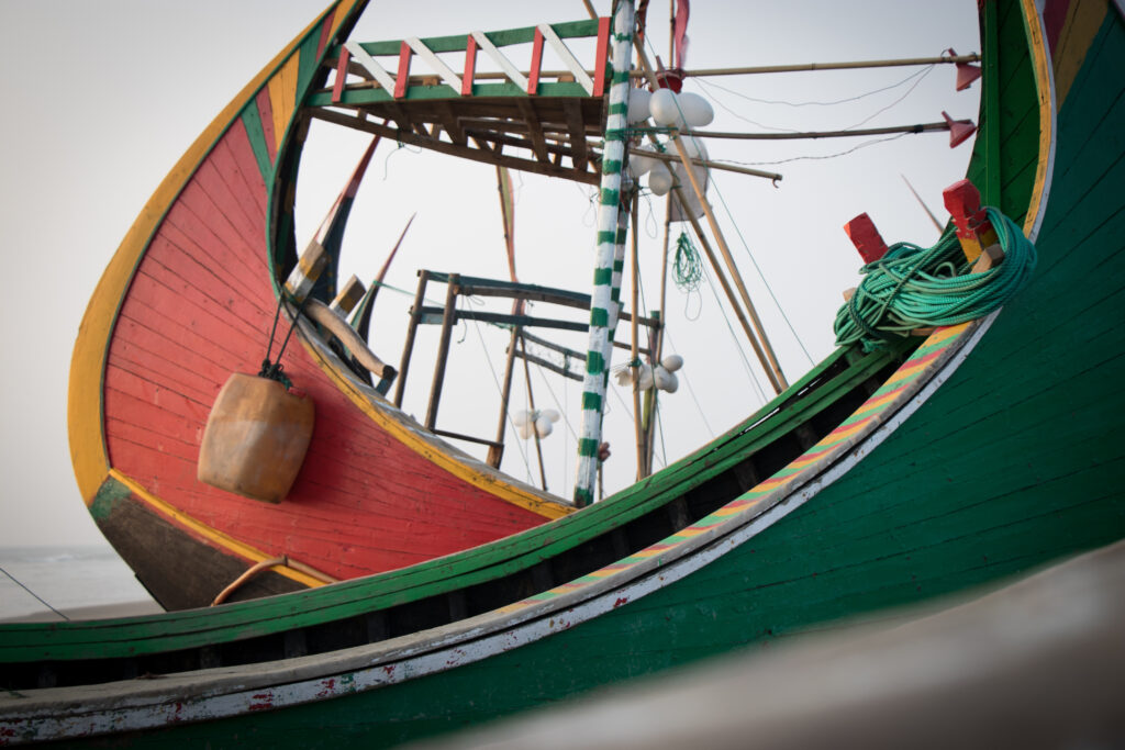 A green moon boat with multicolored trim crosses the foreground in front of a vivid red boat with yellow trim.
