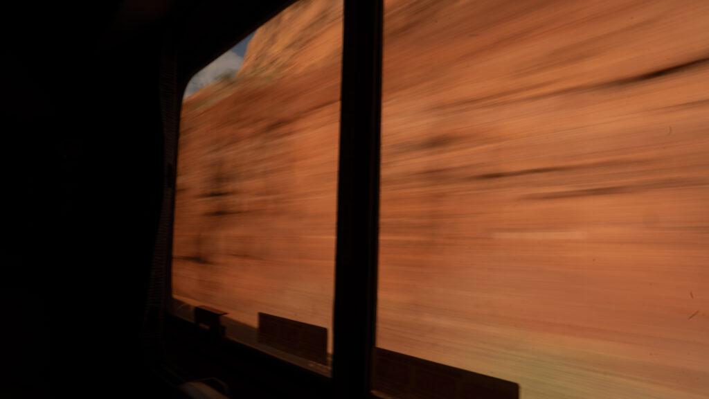 Long exposure image of red rock blurring past the train window, creating streaks of color and motion.