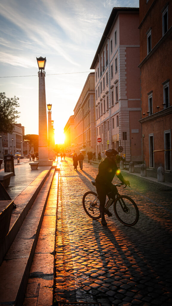Cyclist casting long shadow on cobblestone street at sunrise near Vatican City