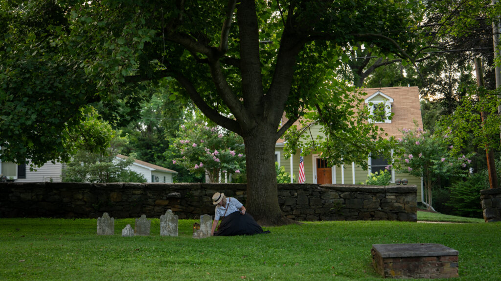 Janet Hughes kneels beside an old headstone and clears debris from the grave in a historic Shepherdstown cemetery.