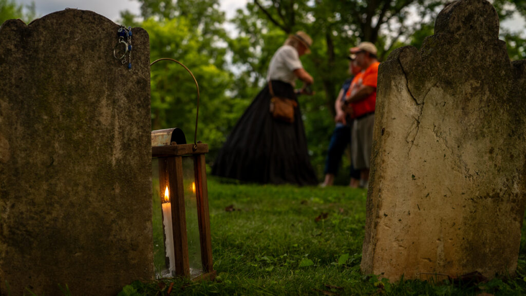 Between cemetery headstones, Janet Hughes shows guests photographs associated with reported spirits in Shepherdstown.